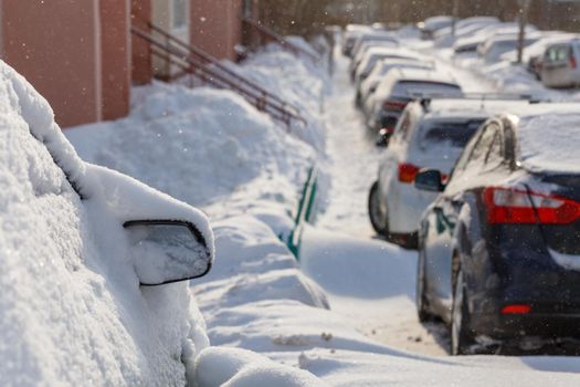 cars buried under snow in parking near residental building at sunny day light - close-up with selective focus