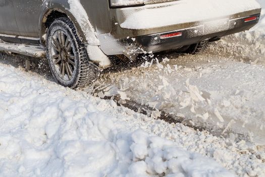 Road snow flies up from a vehicle's spinning wheel. Car's wheels spin and spew up pieces of snow it attempts to gain traction on the slippery road at winter daytime.