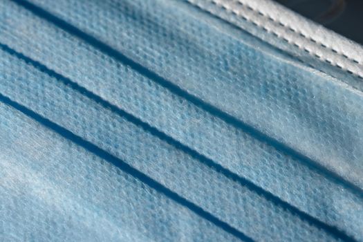 Blue dimpled texture and folds of a disposable 3-ply medical face mask. Mandatory use for many people in public spaces due to Covid aka coronavirus.