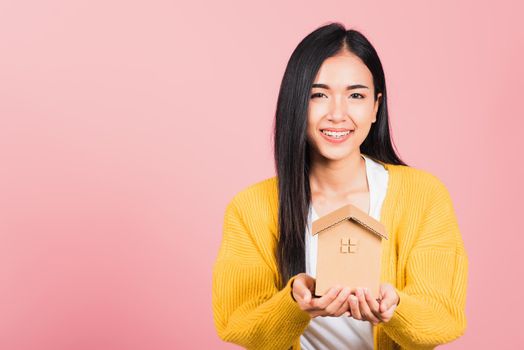 Happy Asian portrait beautiful cute young woman excited smiling holding house model on hand, studio shot isolated on pink background, broker female hold home real estate insurance and banking concept