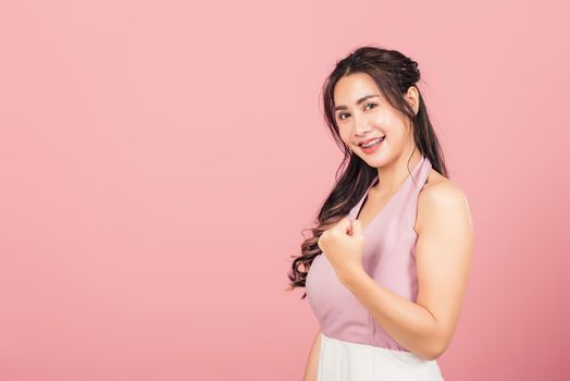 Happy Asian portrait beautiful cute young woman stand makes raised fists up celebrating her winning success gesture, studio shot isolated pink background, Thai female excited say yes! with copy space