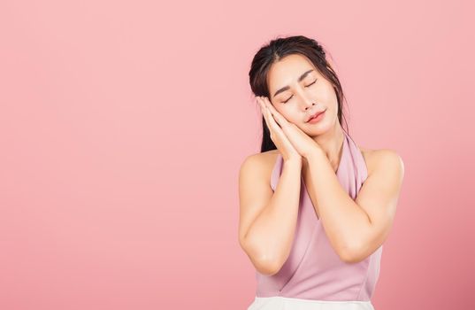 Portrait Asian beautiful young woman pretended emotions sleeping tired eyes closed dreaming with hands together near face, studio shot on pink background, with copy space, insomnia concept