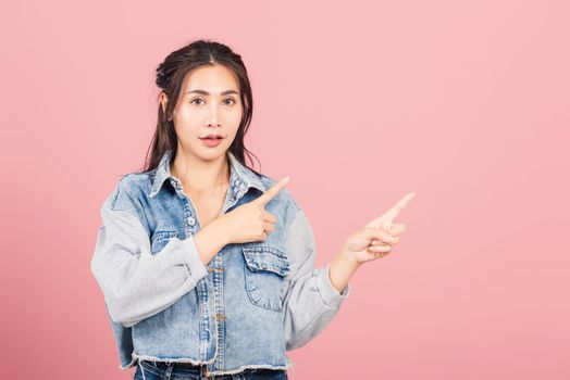 Asian happy portrait beautiful cute young woman wear denim standing pointing finger side away presenting product looking to camera, studio shot isolated on pink background with copy space