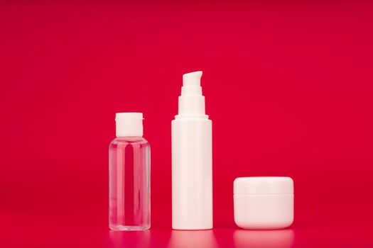 Skin care products against red background. Lotion, face cream and under eye cream set. Concept of beauty cosmetics for daily use