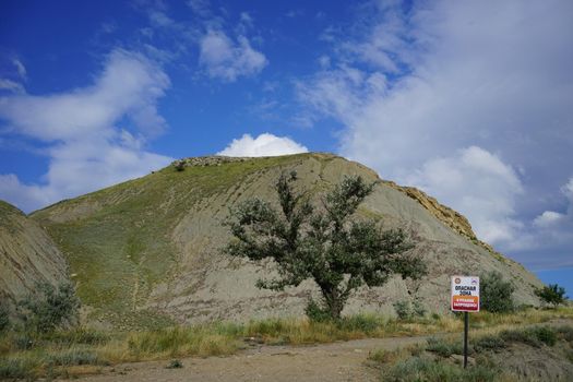 landscape with high hills and a tree on the background of prohibition sign and a blue sky with large white clouds