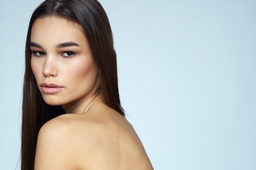 Pretty brunette with bared shoulders long hair body care blue background. High quality photo