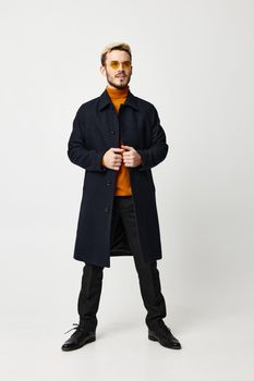 fashionable man in a dark coat spread his legs shoulder-width apart on a light background and an orange sweater model. High quality photo