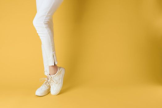 Female feet white sneakers attractive look fashion yellow background. High quality photo