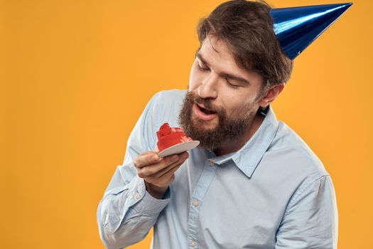 a man with a birthday cake in his hands and in a cap on a yellow background on his birthday. High quality photo