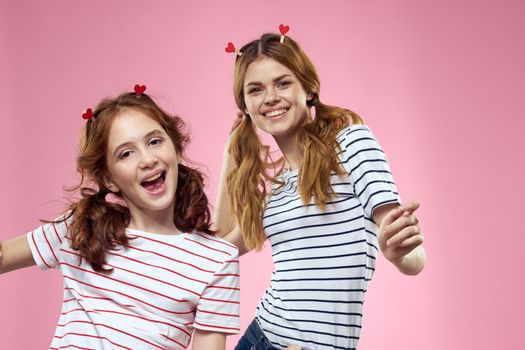 Happy sisters are having fun on a pink background and heart-shaped clothespins on their heads. High quality photo
