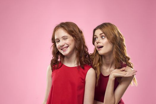 Cheerful mom and daughter wearing red dresses are standing next to joy family on pink background. High quality photo