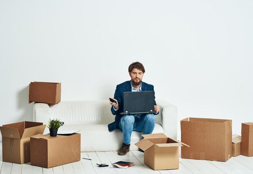 A man sits on the couch in front of a laptop working boxes with things unpacking a new office. High quality photo