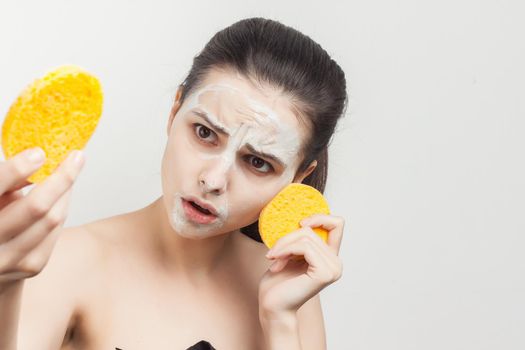 cheerful brunette with bare shoulders face mask sponges in hands skin care. High quality photo