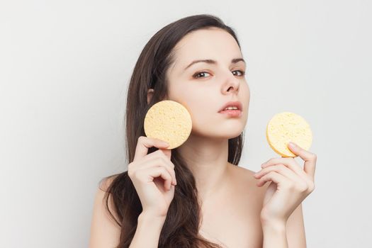 brunette naked shoulders wipes her face but clean skin with a sponge. High quality photo