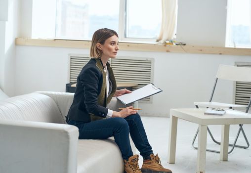 A woman in a suit is sitting on the couch with documents near the window. High quality photo