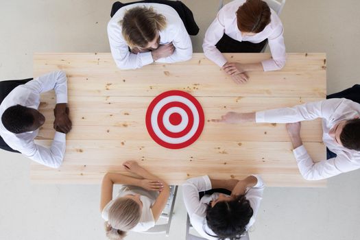 Team of business people pointing at red goal target at meeting table aiming strategic marketing on dartboard bullseye targeted creative idea achievement strategy development concept