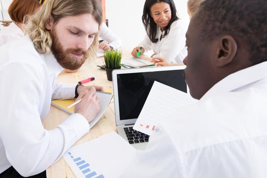 Diverse executive business people team discussing work results at meeting, multiracial businessmen talking analyzing financial statistics report sitting together in modern office with laptop and documents