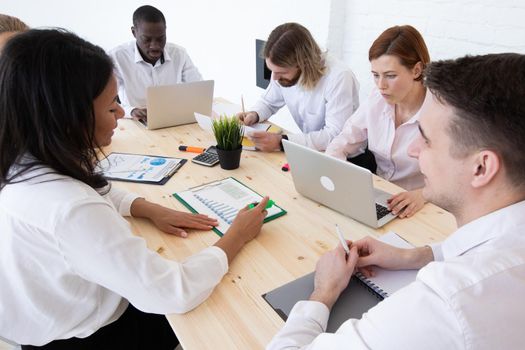 Diverse executive business people team discussing work results at meeting, multiracial businessmen talking analyzing financial statistics report sitting together in modern office with laptop and documents