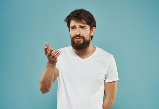 A brunette guy with a thick beard on a blue background gestures with his hands cropped view. High quality photo