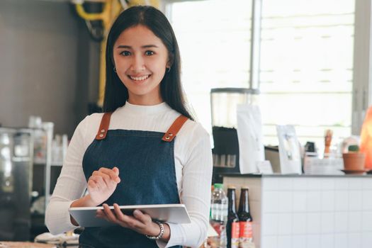 Portrait of woman small business owner using digital tablet and standing in front of counter bar in coffee shop.