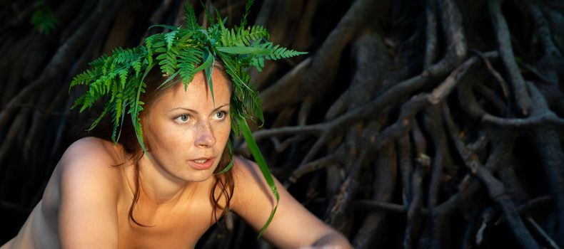 A beautiful young nude woman with fern wreath on her head enjoying nature in the forest river