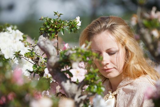 Portrait of a blond girl among the flowers of azalea in the rays of sunlight