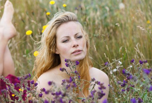 Artistic portrait of freckled woman on natural background. Young woman enjoying nature among the flowers and grass. Close up summer portrait 