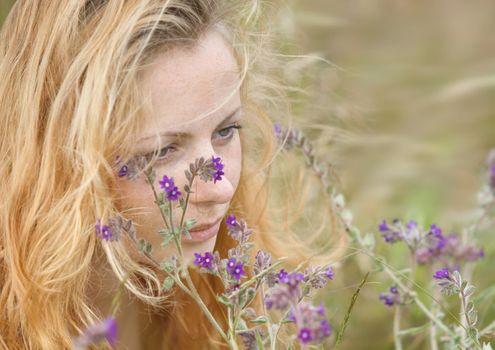 Artistic portrait of freckled woman on natural background. Young woman enjoying nature among the flowers and grass. Close up summer portrait 