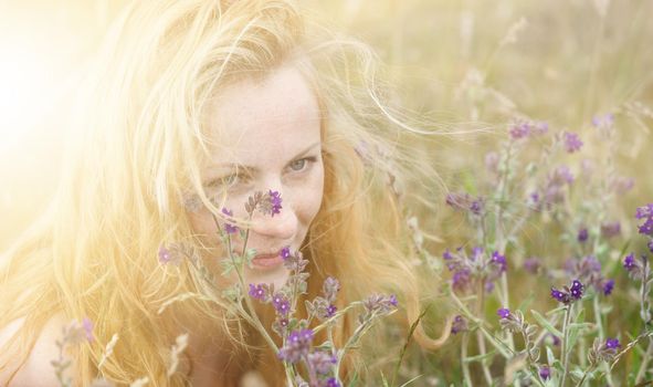 Artistic portrait of freckled woman on natural background. Young woman enjoying nature among the flowers and grass. Close up summer portrait 