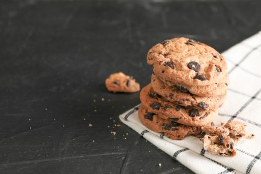 Stack of tasty chocolate chip cookies on napkin and wooden background. Space for text