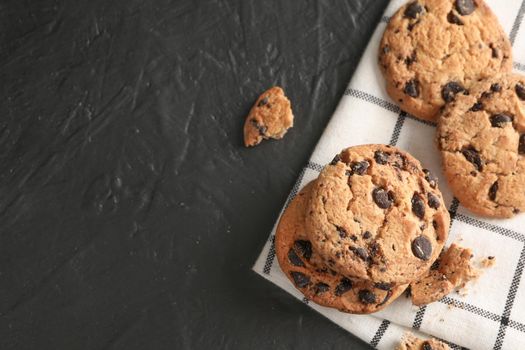 Stack of tasty chocolate chip cookies on napkin and wooden background, top view. Space for text