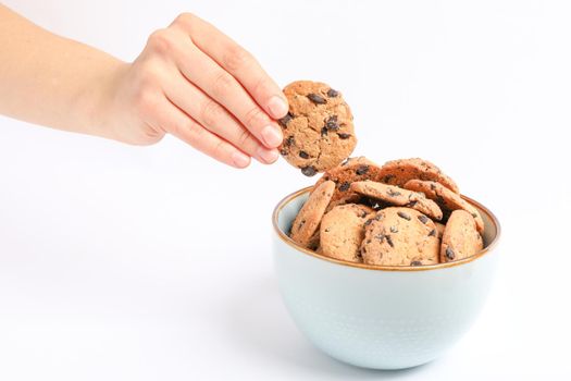 Young woman holding tasty chocolate chip cookie over bowl on white background, closeup