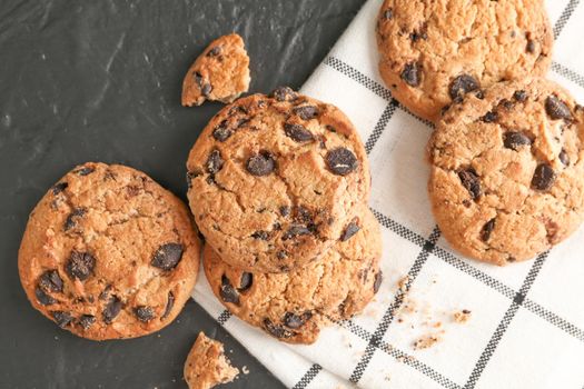 Stack of tasty chocolate chip cookies on napkin and wooden background, top view. Space for text