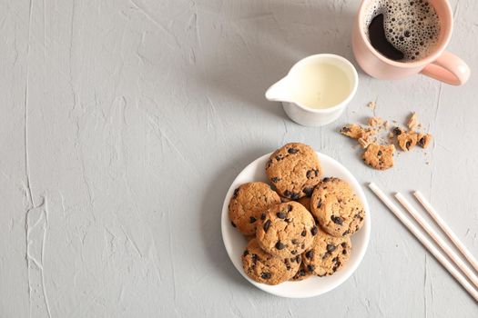 Plate with tasty chocolate chip cookies and cup of coffee on gray background, top view. Space for text