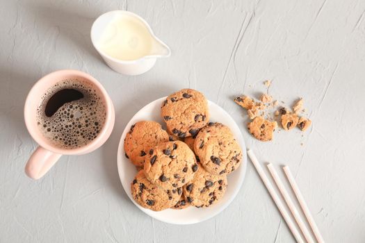 Plate with tasty chocolate chip cookies and cup of coffee on gray background, top view