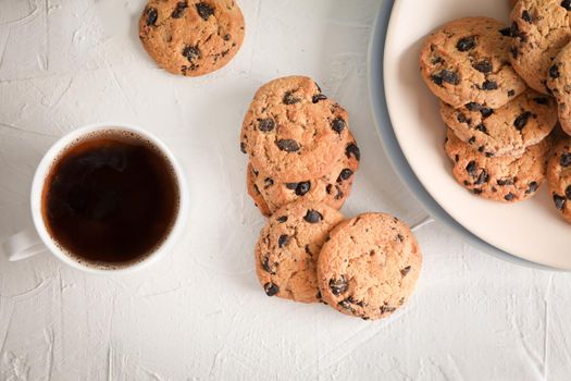 Plate with tasty chocolate chip cookies and cup of coffee on gray background, top view