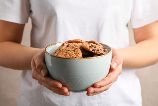 Woman holding bowl with tasty chocolate chip cookies, closeup