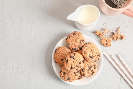 Plate with tasty chocolate chip cookies and cup of coffee on gray background, top view. Space for text