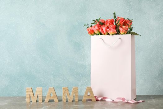 Gift bag with bouquet of pink roses and inscription Mom on grey table against light background