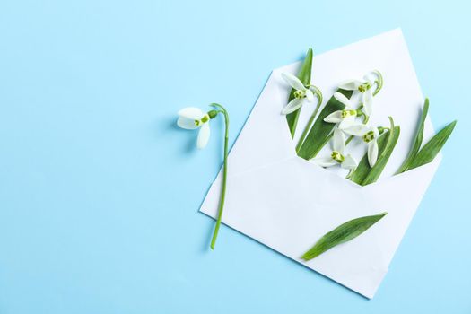 Envelope with snowdrop flowers on color background, space for text