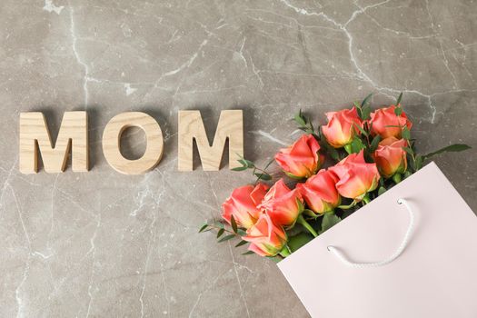 Gift bag with bouquet of orange roses and inscription Mom on brown background, top view