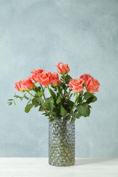 Vase with orange roses on white table against light background