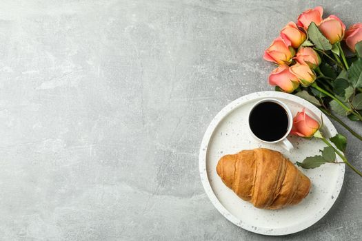 Composition with marble tray, cup of coffee, croissant, roses and space for text on grey background, top view