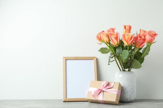 Vase with roses, gift and empty frame on grey table against white background, space for text