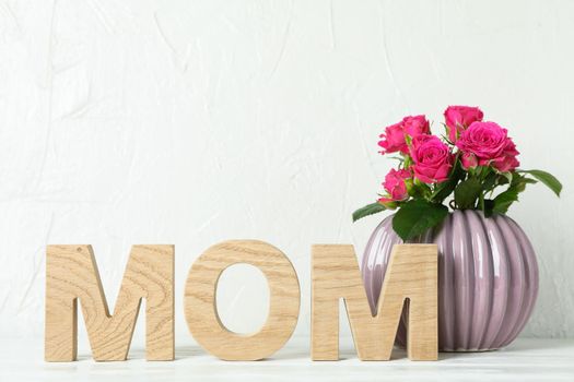 Inscription Mom and vase with pink roses on white table, space for text