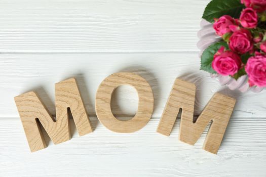 Composition with inscription Mom and pink roses on white wooden background, top view