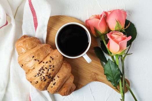 Composition with croissant, cup of coffee, roses and kitchen towel on white background, top view