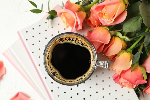 Composition with cup of coffee, notebooks and pink roses on white background, top view