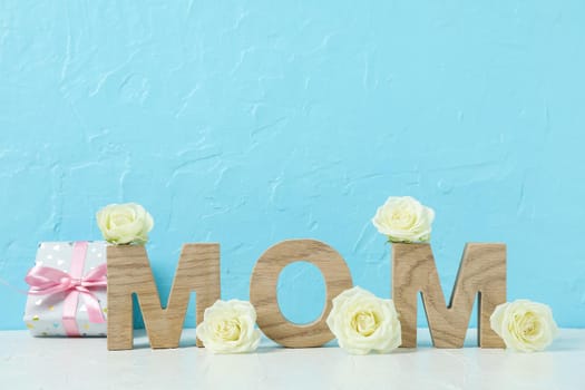 Inscription Mom with white roses on pink table against color background, space for text