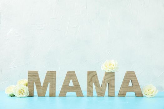 Inscription Mom with white roses on blue table against white background, space for text